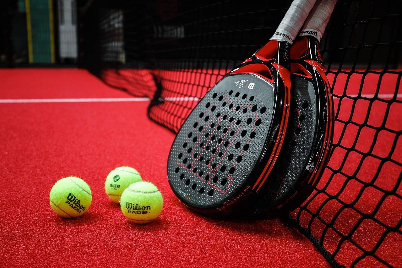 Bild på två padelrack som står lutade mot nätet. Två bollar ligger framför. Står i en hall där du kan spela padel i Göteborg